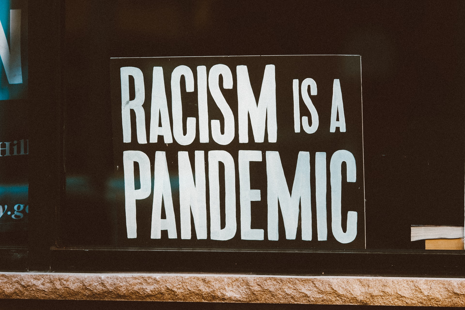 Image shows a black sign with white letters stating "Racism is a pandemic" in capital letters.